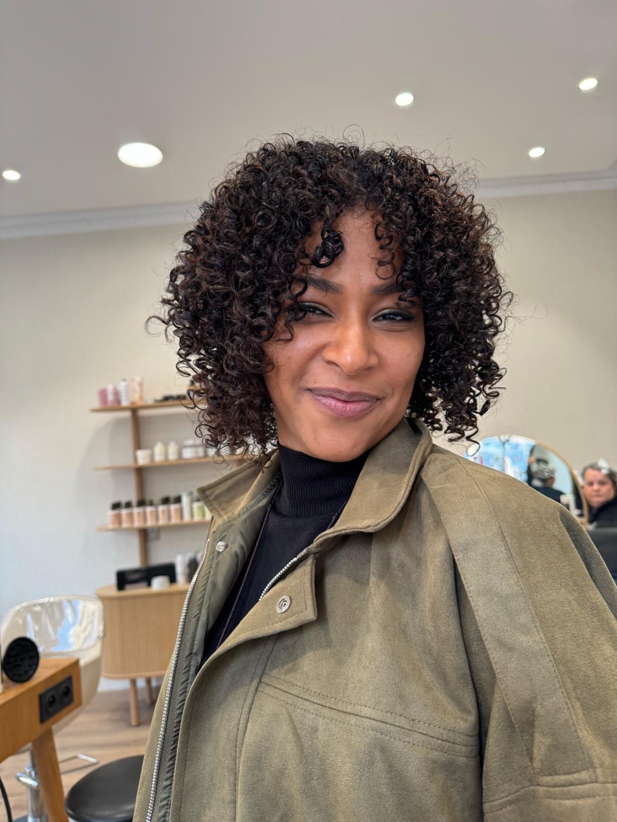 Coupe Curly mi-longue avec frange bouclée volumineuse