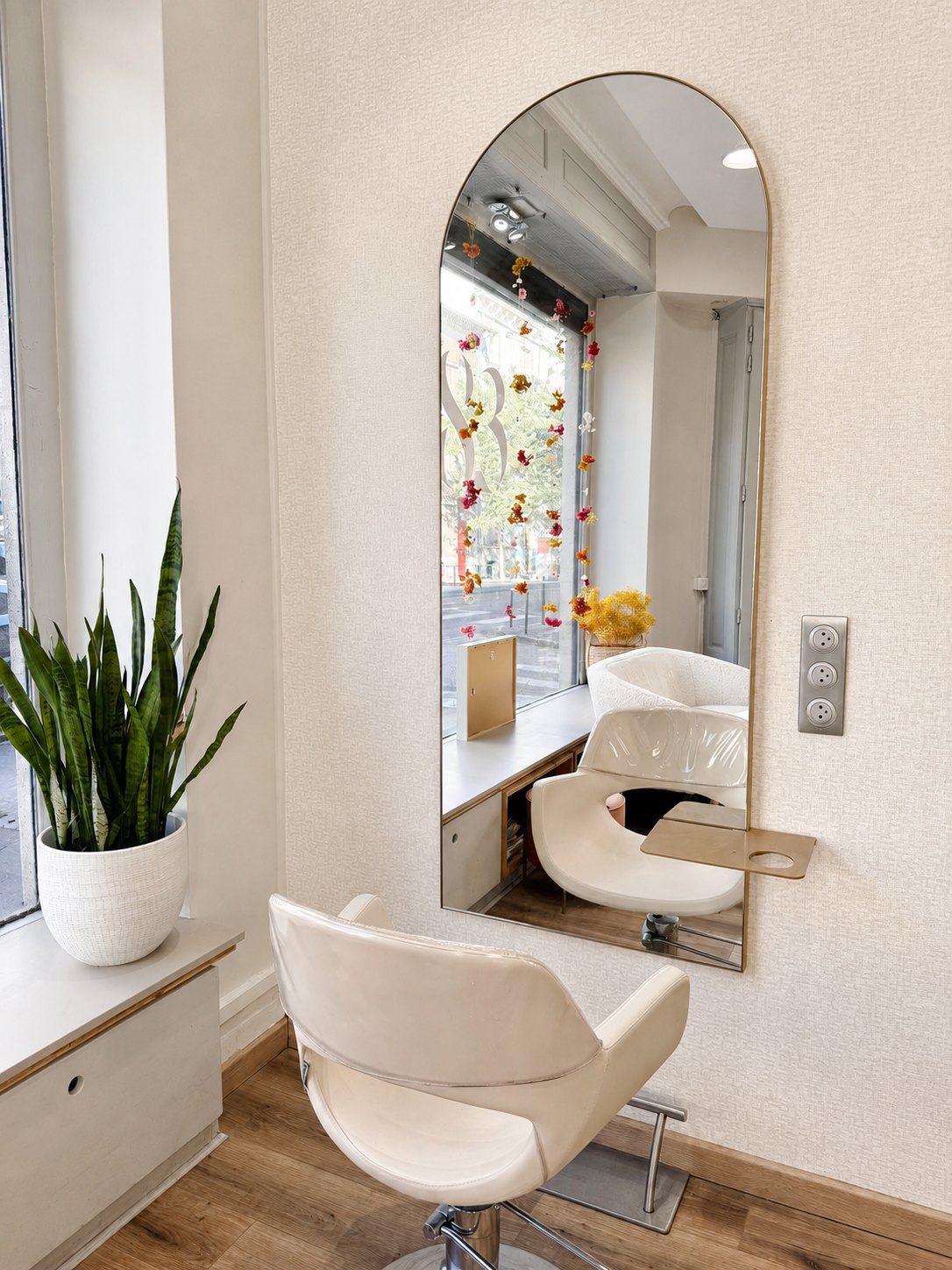 Détail d'un poste de coiffage du salon Le 83 à Nancy : miroir arrondi, fauteuil blanc et plante verte