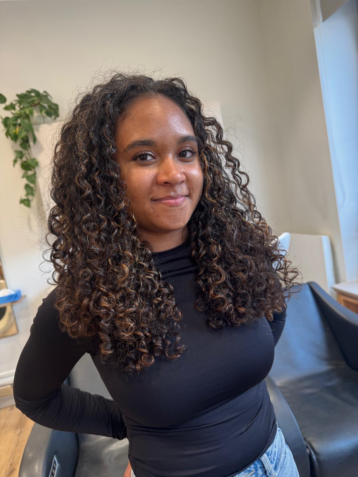 Cheveux bouclés longs bruns avec reflets caramel réalisés au salon